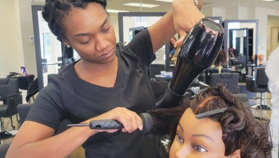 Cosmetology & Hairstyling student blow drying her mannequin head's hair